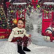 Vada is registered to the contest to win money with this photo: child, toddler, smiling, christmas, holiday, festive, decorations, snowman, tree, gift, winter, background, red, white, green, sweater, skirt, boots, indoor, portrait