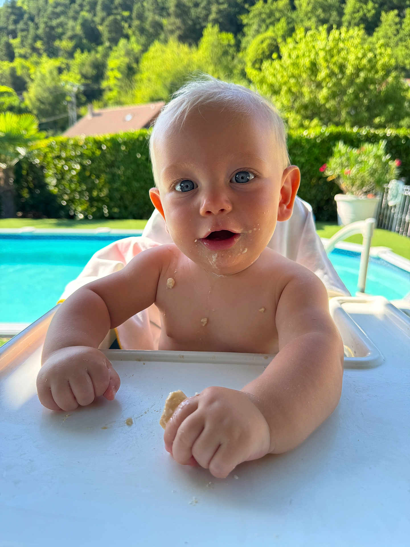Sandro participe au concours pour gagner de l'argent avec cette photo : baby, child, high_chair, food, crumbs, outdoor, pool, greenery, sunlight, face, hands, blue_eyes, skin, summer, nature, happy, sitting, cute, portrait, daytime