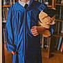 achievement, blue_gown, books, bookshelf, celebration, child, cute, education, formal_clothing, graduation_cap, graduation_gown, indoor, library, person, portrait, smile, teddy_bear, toy, wooden_floor, young_child