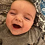 baby, smiling, laughing, face, child, toddler, gray_shirt, bedspread, pattern, blue, black, happy, closeup, infant, young_child, lying_down, eyes_closed, cheerful, indoor, person