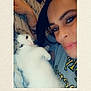 person, cat, selfie, indoor, bed, striped_bed_sheet, tattoo, nose_ring, white_cat, tabby_cat, close_up, smiling, relaxed, snuggling, cute, fluffy, portrait, cozy, kiss_mark, casual