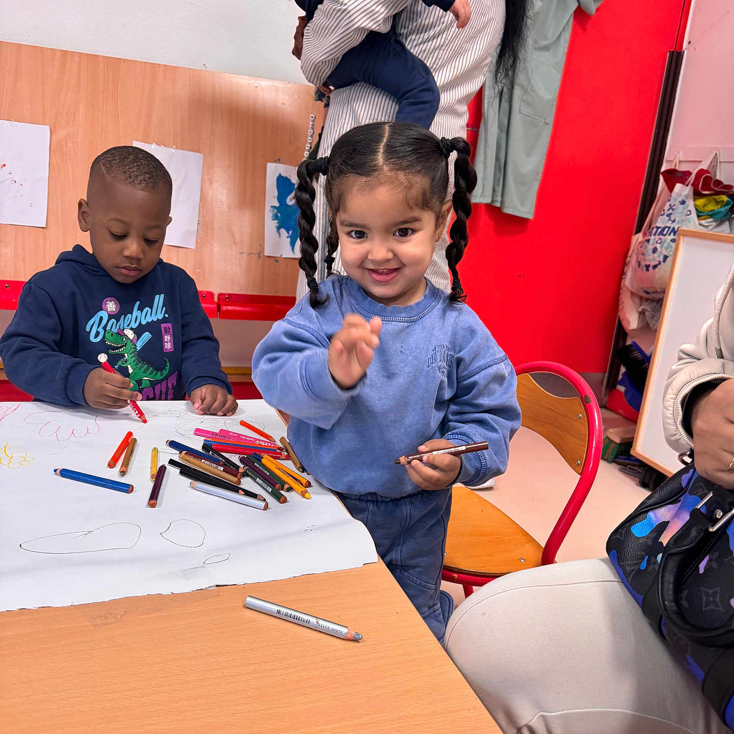 Elyne participe au concours pour gagner de l'argent avec cette photo : child, children, toddler, drawing, crayons, table, chair, woman, baby, indoor, artwork, clothing, smile, hair, person, playroom, red_wall, wooden_furniture, pigtails, casual_wear