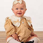 Melania is registered to the contest to win money with this photo: baby, child, smiling, sitting, headband, dress, lace, collar, socks, shoes, floor, indoor, portrait, cute, happy, infant, fashion, young_child, studio, person