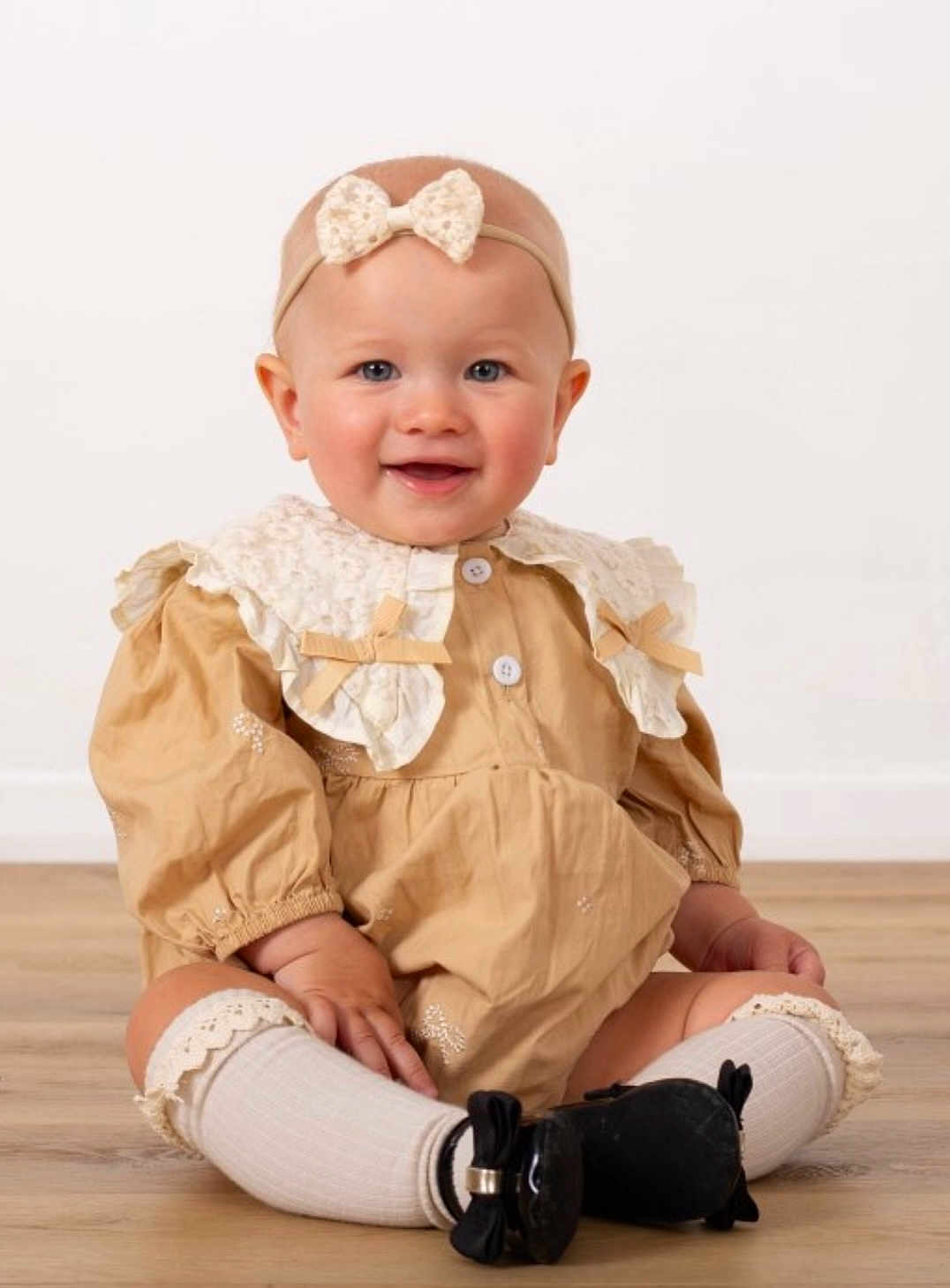 Melania is registered to the contest to win money with this photo: baby, child, smiling, sitting, headband, dress, lace, collar, socks, shoes, floor, indoor, portrait, cute, happy, infant, fashion, young_child, studio, person