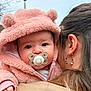 baby, pacifier, pink_hoodie, bear_ears, woman, earring, long_hair, outdoor, streetlamp, hand, face, clothing, portrait, closeup, child, winter_wear, cute, soft_texture, curious, person