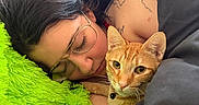 Colby is registered to the contest to win money with this photo: person, cat, sleeping, glasses, blanket, orange_tabby, collar, tattoo, pillow, green, bedroom, indoor, resting, close_up, comfort, calm, feline, pet, relaxation, natural_light
