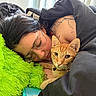 person, cat, sleeping, glasses, blanket, orange_tabby, collar, tattoo, pillow, green, bedroom, indoor, resting, close_up, comfort, calm, feline, pet, relaxation, natural_light