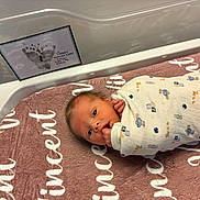 Vincent is registered to the contest to win money with this photo: newborn, baby, infant, swaddle, blanket, hospital_bassinet, footprint, frame, face, hand, bed, soft_toys, hospital, cute, wrapped, lying_down, portrait, indoor, person, toddler