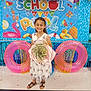 child, girl, smiling, dress, sandals, bouquet, balloons, inflatable_ring, backdrop, party, celebration, floor, decoration, summer, pool_theme, happy, indoor, event, colorful, flower