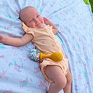Delia joined the competition — help win amazing prizes! baby, infant, blanket, unicorn_pattern, outdoor, grass, onesie, peach_color, toy, rattle, smile, happy, relaxed, child, cute, lying_down, pastel_colors, playtime, soft_texture, nature