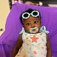 Aaleigha is registered to the contest to win money with this photo: accessory, baby, child, clothing, colorful, curly_hair, cute, expression, face, furniture, indoor, infant, pacifier, person, portrait, purple_chair, seated, starfish_outfit, sunglasses, toy