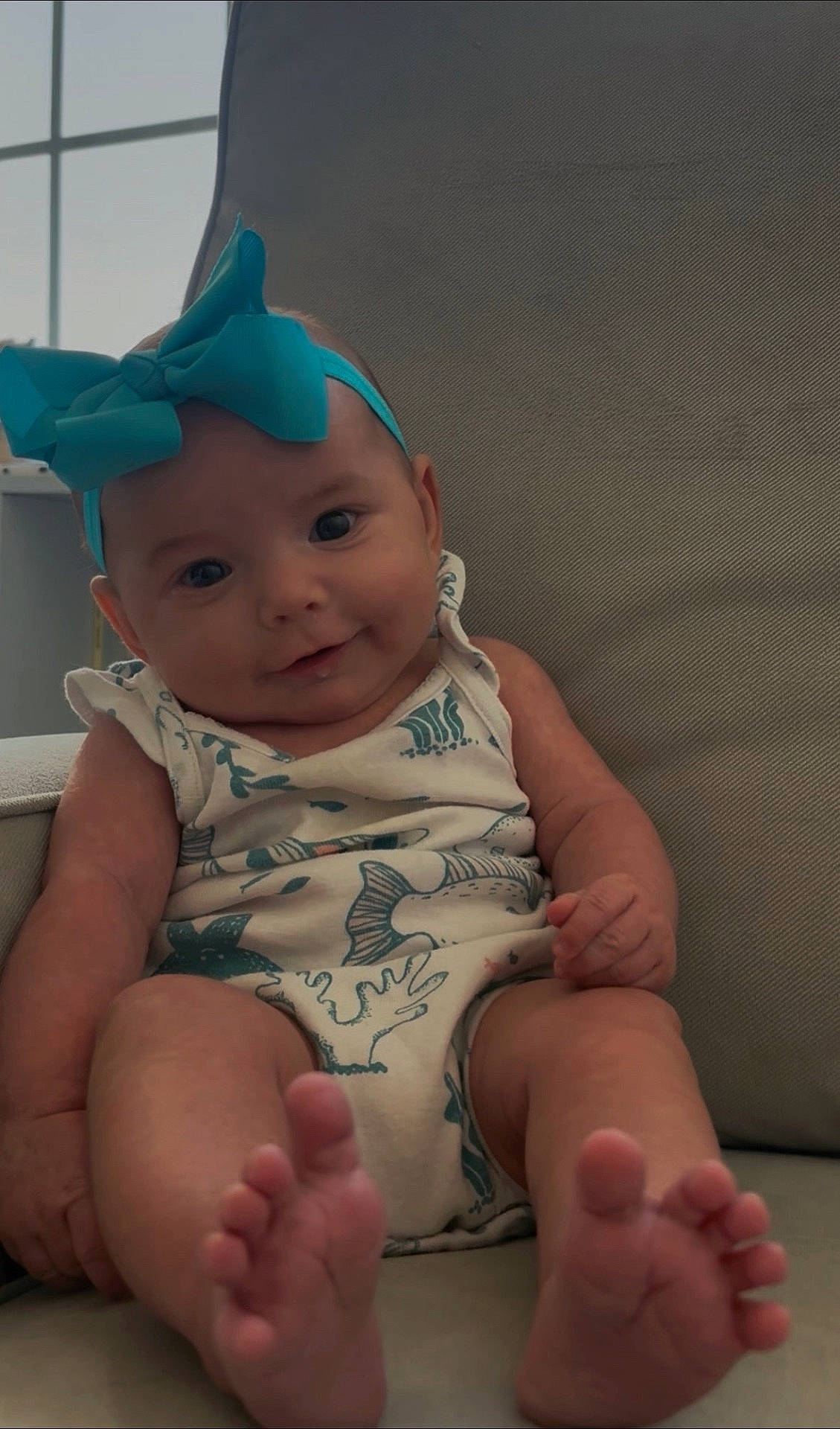 baby, blue_bow, chair, child, closeup, cute, feet, fish_pattern, happy, headband, indoor, infant, legs, natural_light, onesie, portrait, sitting, skin, smiling, window