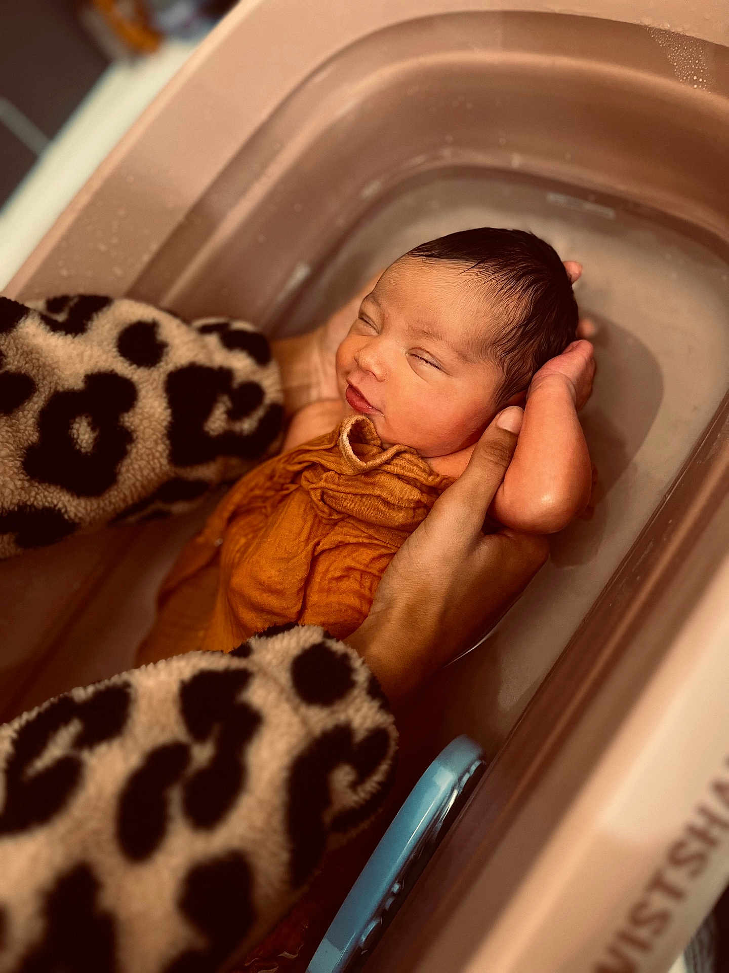 Giulia participe au concours pour gagner de l'argent avec cette photo : newborn, baby, infant, bath, tub, hands, cloth, orange_cloth, leopard_print, sleeves, water, skin, face, closed_eyes, sleeping, gentle, care, tenderness, indoors, portrait