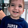 Asher is registered to the contest to win money with this photo: child, toddler, smiling, laughing, portrait, face, teeth, brown_hair, blue_shirt, text_on_clothing, super_cool_dude, outdoor, porch, railing, shutters, adult_hand, family, happy, closeup, daylight