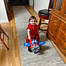 toddler, child, smiling, red_outfit, toy_airplane, toy_vehicle, indoor, hallway, home, wooden_floor, rug, furniture, barstool, dresser, portrait, sitting, happy, playtime, brown_hair, family_home