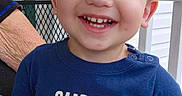 Asher joined the competition — help win amazing prizes! child, toddler, boy, smiling, portrait, outdoor, porch, blue_shirt, t_shirt, text_on_clothing, happy, teeth, brown_hair, blue_eyes, adult_hands, chair, house, daylight, close_up, casual