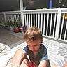 balcony, blue_shirt, brown_hair, child, clothing, flowers, lap, looking_down, outdoor, person, pillows, plants, porch, portrait, railing, red_toy, short_hair, sitting, toddler, toy_car