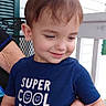 adult_hands, balcony, blue_shirt, boy, brown_hair, child, happy, house, outdoor, painted_nails, porch, portrait, railing, shutter, sitting, smiling, super_cool_dude, text_on_clothing, toddler, white_siding