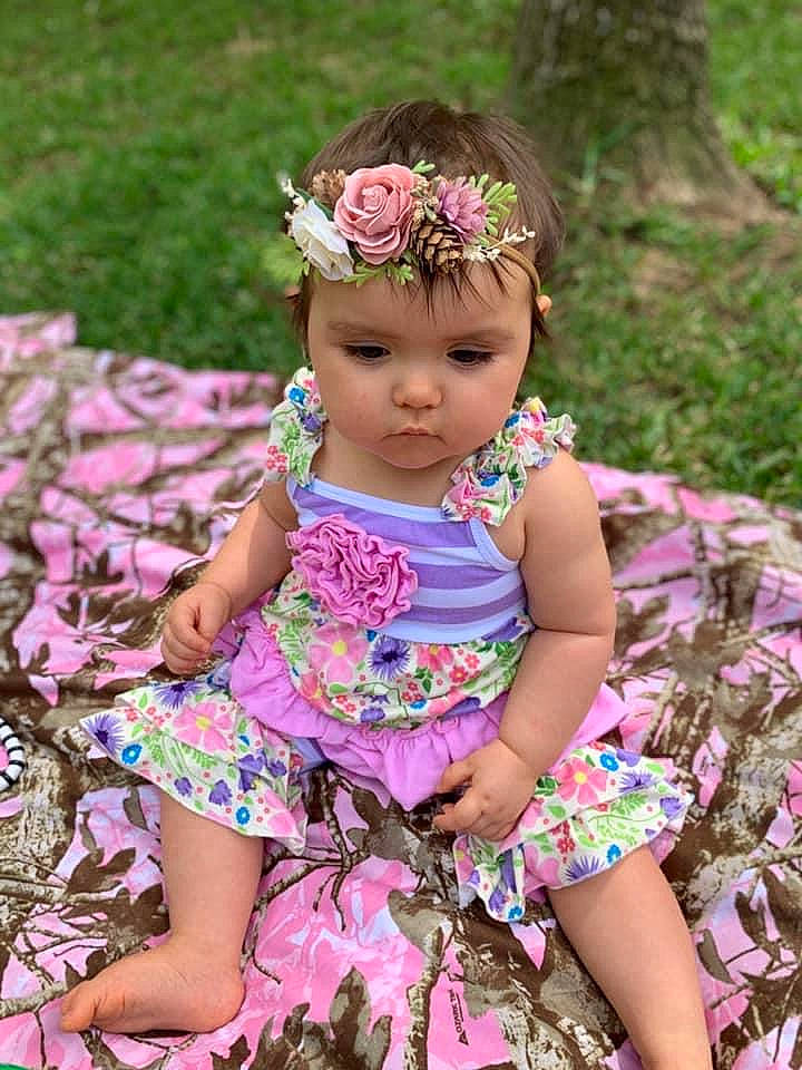 Paisley is registered to the contest to win money with this photo: baby_toddler_clothing, botany, clothing, day_dress, dress, eye, face, flower, grass, happy, head, headwear, leaf, magenta, people_in_nature, person, pink, plant, purple, skin