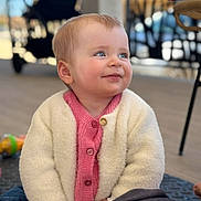Lya a rejoint le concours — aidez-le/la à gagner de superbes lots ! baby, child, smiling, cardigan, pink, white, sitting, floor, indoor, portrait, happy, cute, person, blonde_hair, blue_eyes, toy, furniture, table, chair, stroller