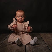 Thalia a rejoint le concours — aidez-le/la à gagner de superbes lots ! baby, child, infant, dress, beige, sitting, wooden_floor, dark_background, portrait, cute, small_hands, curious, studio, indoor, young, person, clothing, footwear, sock, expression