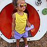 Kora joined the competition — help win amazing prizes! toddler, child, sunglasses, yellow_tank_top, purple_shorts, pink_sneakers, playground, playground_equipment, red_tunnel, wood_chips, outdoor, person, fashion, accessory, handbag, reflection, curly_hair, confident, summer, casual