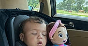 Kora joined the competition — help win amazing prizes! blue_overalls, car_interior, car_seat, child, clouds, daytime, doll, headband, infant, nature_outside, pink_shirt, relaxation, safety_harness, seatbelt, sleeping, sunlight, toddler, toy, trees, window