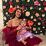 Kora joined the competition — help win amazing prizes! baby, burgundy_dress, celebration, child, couch, dress, floral_wall, flower_crown, flowers, happy, head_accessory, holding, indoor, person, portrait, purple_dress, seated, smile, tattoo, woman