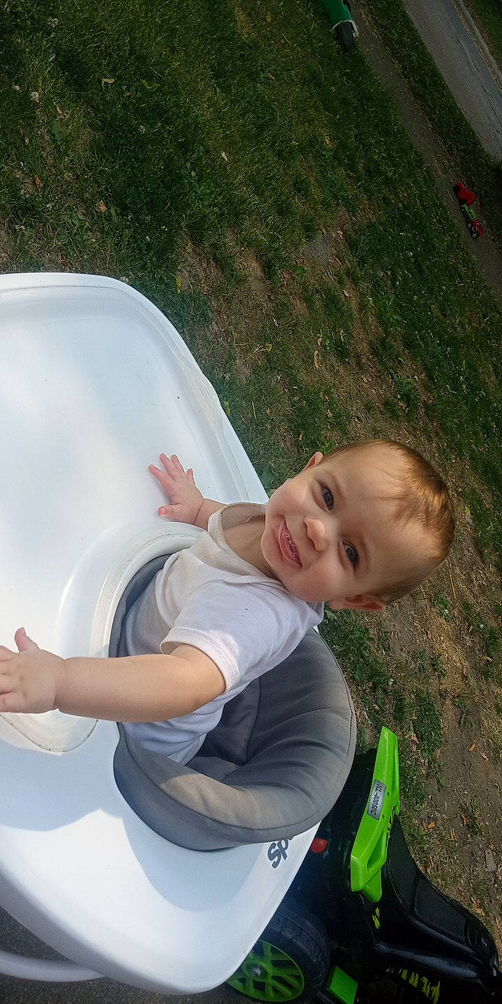 John is registered to the contest to win money with this photo: automotive_exterior, chair, child, comfort, elbow, fun, grass, hairstyle, happy, joy, leg, leisure, people_in_nature, person, play, recreation, sitting, smile, t_shirt, toddler