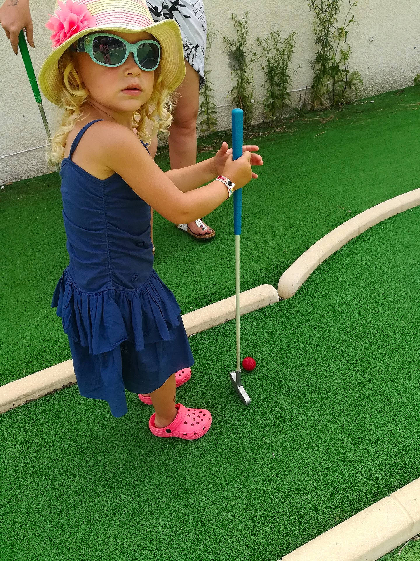 Typhaine a rejoint le concours — aidez-le/la à gagner de superbes lots ! ball_game, child, fun, girl, golf, golf_equipment, grass, green, headgear, headwear, individual_sports, lawn, leisure, miniature_golf, person, plant, play, putter, recreation, shoulder