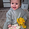 baby, child, infant, girl, smiling, pigtails, flower_bouquet, dandelions, milestone, plaque, sitting, gray_clothing, hoodie, pants, indoor, carpet, happy, cute, portrait, person