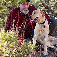 Samson is registered to the contest to win money with this photo: animal, beard, brown_eyes, cap, casual_clothing, collar, daylight, dog, friendship, golden_retriever, grass, leash, man, nature, outdoor, pet, relaxed, sitting, smiling, trees