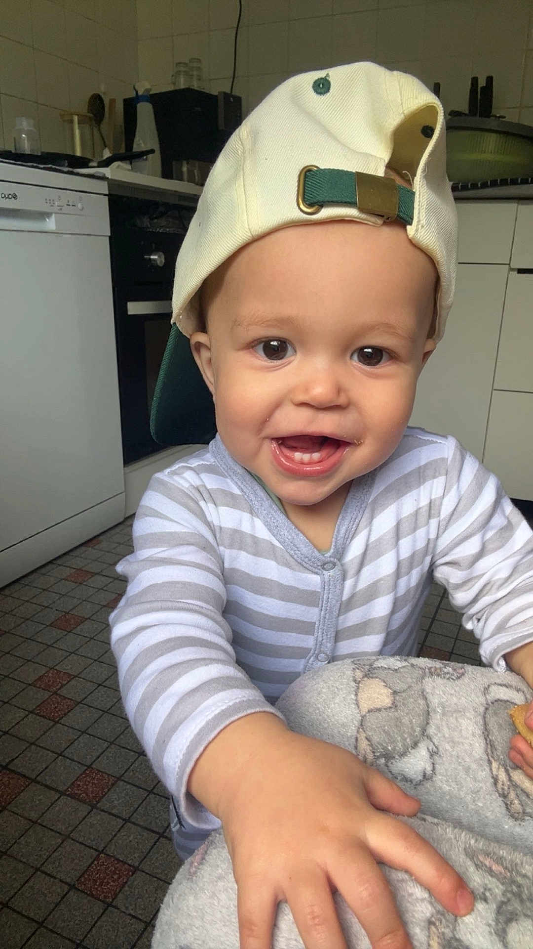 Rémy a rejoint le concours — aidez-le/la à gagner de superbes lots ! toddler, child, baby, cap, hat, striped_clothing, pajamas, smile, happy, indoor, kitchen, floor_tiles, blanket, hand, face, young_child, cute, playful, person, infant