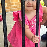 Lakelynne is registered to the contest to win money with this photo: toddler, child, pink_dress, blue_eyes, metal_bars, curious, outdoor, brick_wall, sandals, person, holding, standing, cute, portrait, baby, summer, daylight, footwear, hand, skin