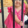 Lakelynne is registered to the contest to win money with this photo: toddler, child, pink_dress, blue_eyes, metal_bars, curious, outdoor, brick_wall, sandals, person, holding, standing, cute, portrait, baby, summer, daylight, footwear, hand, skin