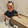 child, toddler, portrait, smiling, kneeling, indoors, wooden_box, number_seven, navy_shirt, suspenders, anchor_pattern, striped_pants, hair_buns, brown_shoes, beige_wall, floor, furniture, hand, looking_at_camera, family_photo