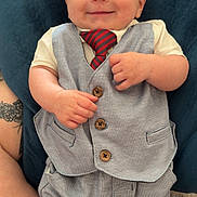 Blake is registered to the contest to win money with this photo: baby, blue_cushion, button, child, clothing, cute, eyes, face, fashion, hands, happy, indoor, infant, person, portrait, sitting, smile, tattoo, tie, vest