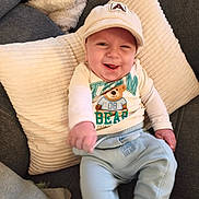 Ayden a rejoint le concours — aidez-le/la à gagner de superbes lots ! baby, infant, smiling, cap, hat, pillow, couch, blanket, teddy_bear, graphic_tee, long_sleeve, sweatpants, cozy, home_interior, cushion, portrait, sitting, happy, cute, hand