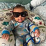 Legend joined the competition — help win amazing prizes! baby, child, sunglasses, dinosaur_pattern, onesie, pillow, animal_print, bed, blanket, tongue_out, smile, indoor, cute, infant, cozy, playful, hand, head, face, person
