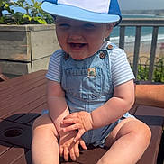 Arlo joined the competition — help win amazing prizes! baby, child, smiling, cap, denim_overalls, outdoor, table, wood, sunlight, beach, sky, plants, hand, foot, person, summer, happy, nature, portrait, seaside