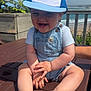 baby, child, smiling, cap, denim_overalls, outdoor, table, wood, sunlight, beach, sky, plants, hand, foot, person, summer, happy, nature, portrait, seaside