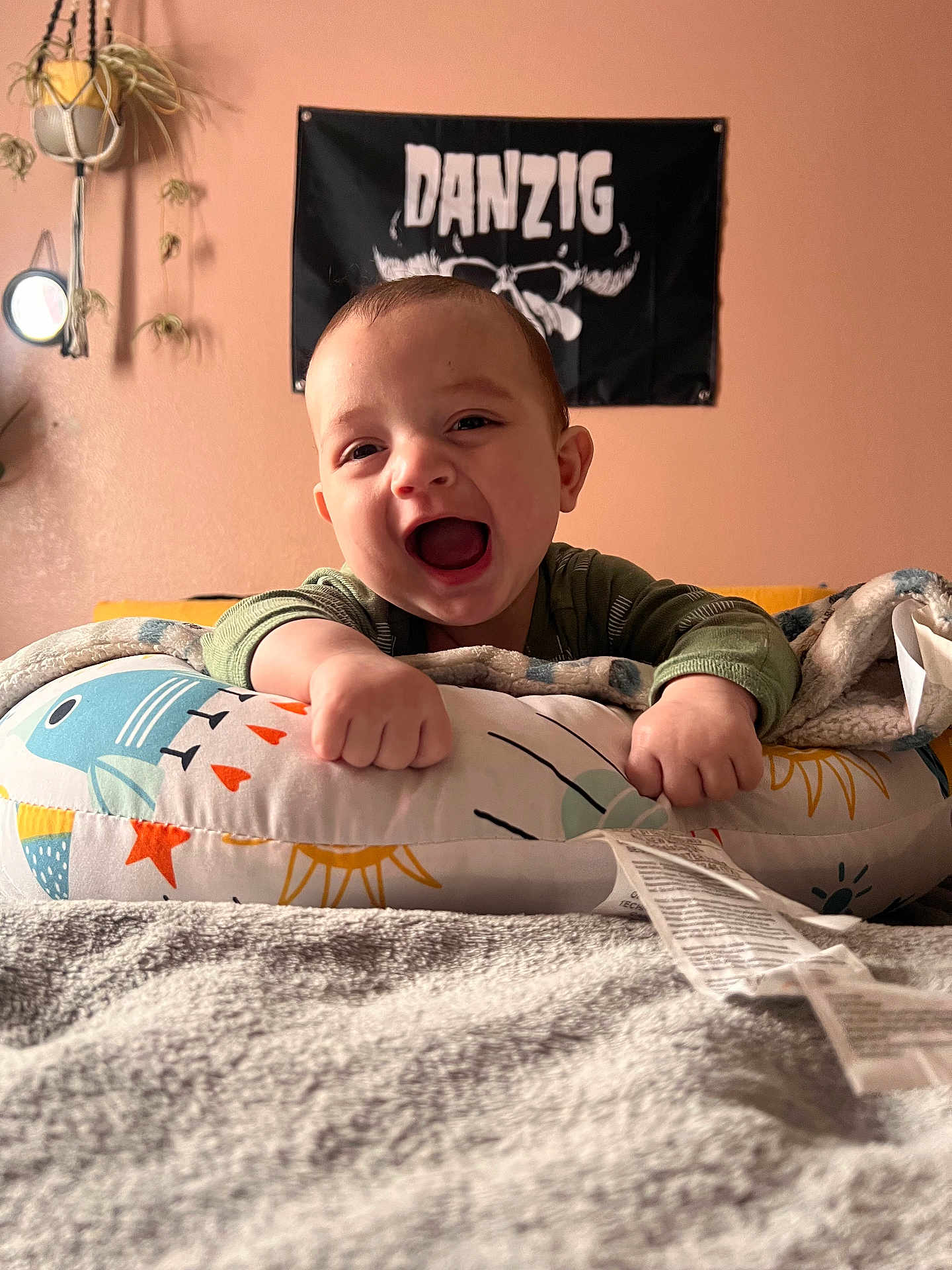 Anthony joined the competition — help win amazing prizes! baby, infant, child, smile, mouth_open, pillow, blanket, bedroom, poster, band_poster, wall, hanging_plant, plants, hands, face, cozy, bedding, portrait, happy, indoor