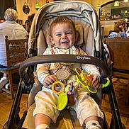 Liam a rejoint le concours — aidez-le/la à gagner de superbes lots ! baby, bib, cafe, chair, child, clothing, face, furniture, happy, head, indoor, lighting, people, seatbelt, smile, socks, stroller, table, toy, wooden_floor