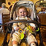 baby, bib, cafe, chair, child, clothing, face, furniture, happy, head, indoor, lighting, people, seatbelt, smile, socks, stroller, table, toy, wooden_floor