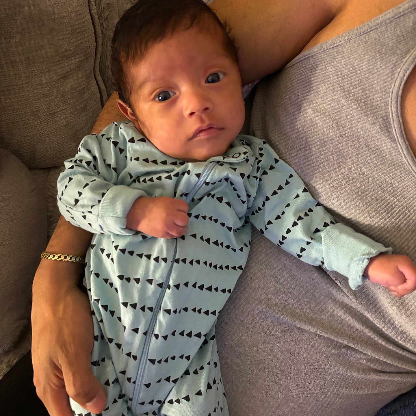 Alexander Torres is registered to the contest to win money with this photo: adult, arm, baby, blue_clothing, casual, closeup, couch, face, gray_clothing, hand, holding, indoor, infant, newborn, onesie, patterned_clothing, person, portrait, relaxing, soft_furniture