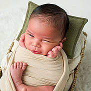 Noham a rejoint le concours — aidez-le/la à gagner de superbes lots ! newborn, baby, swaddle, wicker_basket, green_pillow, winking, infant, skin, foot, hand, wrapped, cute, resting, indoors, soft_texture, fluffy_background, portrait, closeup, sleepy, peaceful