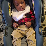 Kingston S Hicks is registered to the contest to win money with this photo: baby, infant, child, toddler, car_seat, bib, plaid_shirt, checkered_shirt, khaki_pants, socks, hands, face, eyes, looking_at_camera, indoor, carpet, floor, cozy, portrait, dark_hair