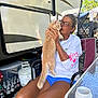 Mr Sam is registered to the contest to win money with this photo: affection, beverages, camping, cat, chair, glass_table, glasses, orange_tabby, outdoor, pet, plastic_container, propane_tank, relaxation, rv, shorts, sunlight, table, trees, white_shirt, woman