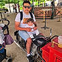 Emily participe au concours pour gagner de l'argent avec cette photo : man, baby, motorcycle, outdoor, sunglasses, stroller, people, greenery, casual_clothing, shorts, tshirt, footwear, handbag, bench, umbrella, brick_wall, metal_railings, daylight, portrait, smile