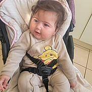 Emily participe au concours pour gagner de l'argent avec cette photo : baby, child, stroller, onesie, winnie_the_pooh, curly_hair, blue_eyes, cushion, seatbelt, indoor, floor_tiles, cute, smiling, infant, clothing, person, portrait, sitting, soft_lighting, baby_girl